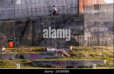 Boy resting on stone bench, friend cycling in background, Berlin, Germany Stock Photo