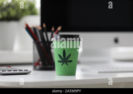 Green coffee cup with cannabis logo on office tabl Stock Photo