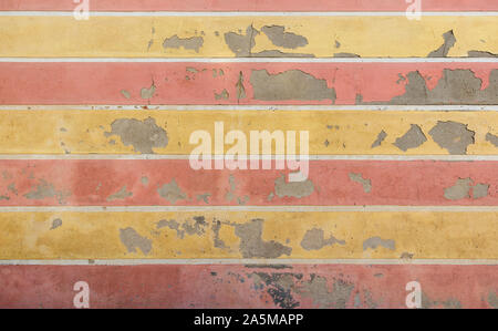 Weathered and old concrete wall with horizontal yellow and red stripes, paint is peeling off. High resolution abstract full frame textured background. Stock Photo