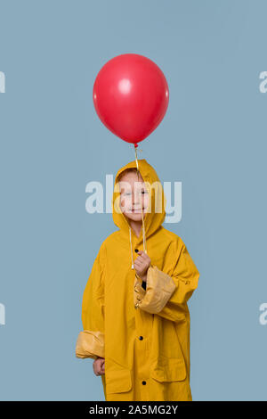 Portrait of the cute boy in a yellow raincoat with a red balloon  Stock Photo