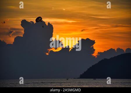 Amazing, wonderful and dramatic golden colored sky behind the clouds during a stunning sunset while tandem parasailers passing through the magical mom Stock Photo