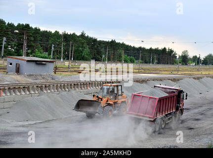 Wheel loader unload gravel and crushed stone in the dump truck. Unloading bulk cargo with of the cargo railway platform in the mining quarry - Image Stock Photo
