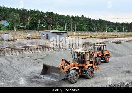 The wheel loader unloads crushed stone in a gravel pit. Unload bulk cargo with of the cargo railway platform in the mining quarry - Image Stock Photo