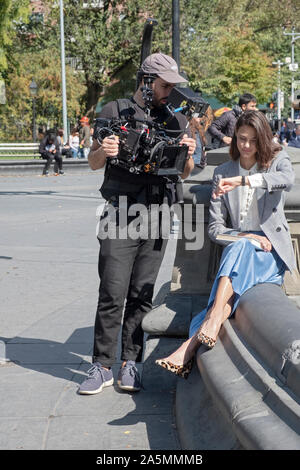 A cinematographer & a model film what appears to be a commercial for watches. At he fountain in Union Square Park Stock Photo