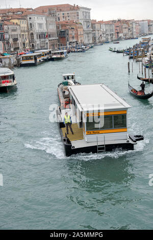 The Piazzale Roma vaporetto station is pushed by a tug boat, likely for repair or refurbishing. From the Rialto Bridge on  the Grand Canal in Venice. Stock Photo