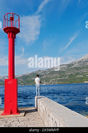 An unidentified young man standing on a precarious spot and fishing in the Adriatic. On the Croatian island of Korcula. Stock Photo