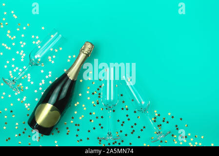 Champagne bottle and three glasses on trendy mint background with golden star shaped confetti. Flat lay style. Holiday concept. Mockup for your design Stock Photo