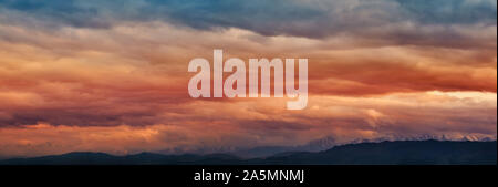 Dramatic light through the clouds against the backdrop of an exciting, vibrant stormy sky at sunset, dawn in the mountains. panorama, natural composit Stock Photo