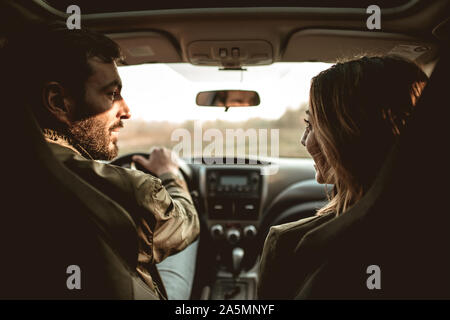Rear view of young beautiful couple sitting on front passenger seats and looking at each other.