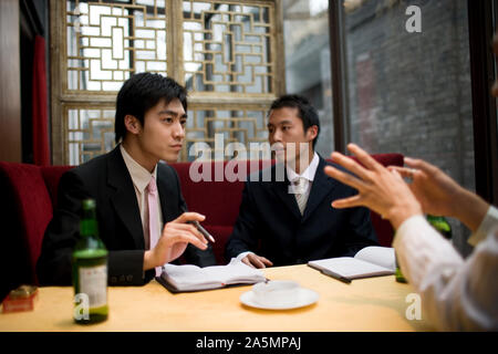 Young adult businessmen sitting at a table in a bar drinking beers and smoking. Stock Photo