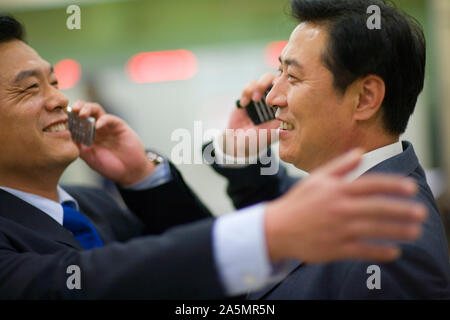 Two smiling businessmen congratulating each other while talking on their cell phones. Stock Photo