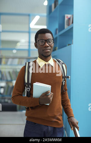 Waist up portrait of smart African-American student holding book standing in college library Stock Photo