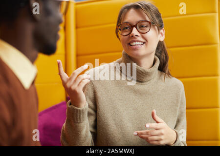 Portrait of pretty young woman talking to friend while relaxing in library lounge, copy space Stock Photo