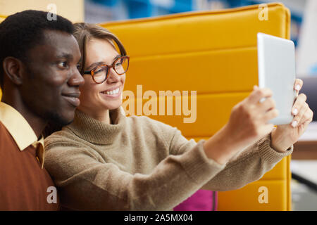 Portrait of two college students taking selfie via digital tablet while relaxing in library lounge, copy space Stock Photo