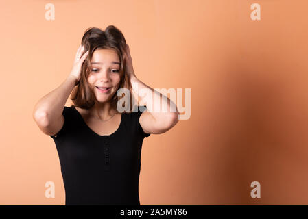 The girl is worried and holds on to her head, on a light orange background. Stock Photo