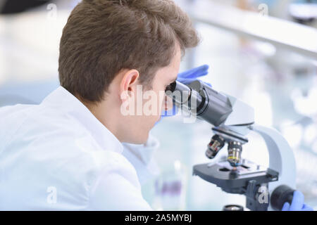 Young male scientist looking through a microscope in a laboratory doing research, microbiological analysis, medicine. Stock Photo
