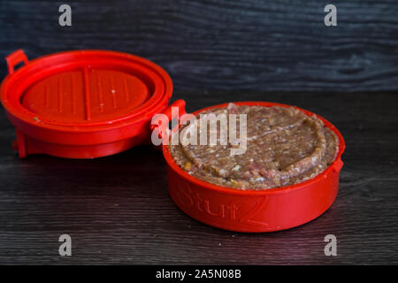 Red plastic burger stuffer. Beef and pork mince patties being stuffed with crispy bacon, chunks of colby cheese. Shows press in use with raw products Stock Photo