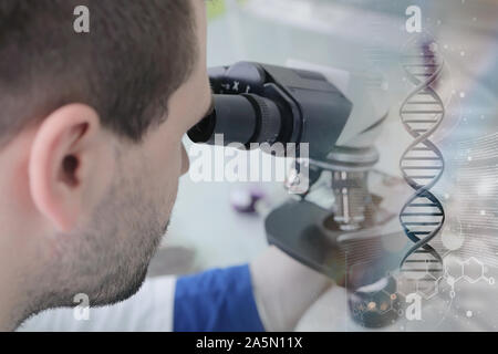 Young male male scientist looking through a microscope in a laboratory doing research, microbiological analysis, medicine. Stock Photo