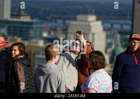 A young couple taking selfies on the Kondiaronk belvedere on Montreals Mont Royal, with the skyscrapers of downtown beyond Stock Photo