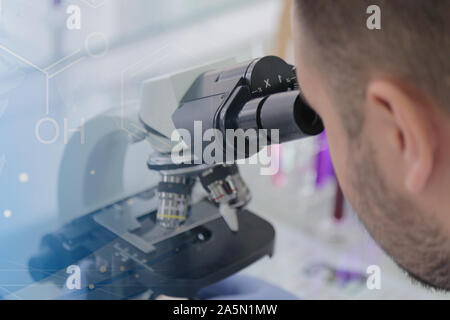 Young male male scientist looking through a microscope in a laboratory doing research, microbiological analysis, medicine. Stock Photo