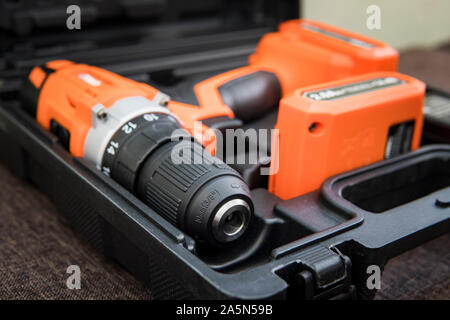 Top view of electric screwdriver on white background. orange screwdriver or drill in a black container lies on the floor. Tool for tightening screws. Stock Photo