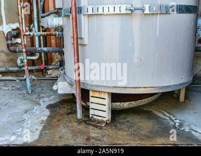 Water heater leaks from the bottom to the floor. Overflowing water heater drip pan. The plumber service for inspection, repair or replacement Stock Photo