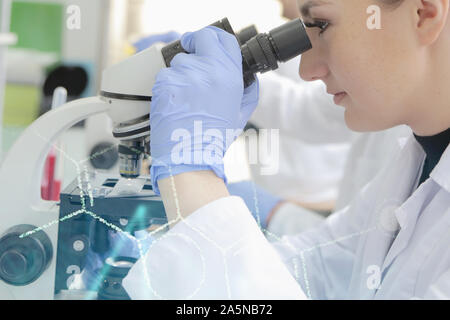 Young female scientist looking through a microscope in a laboratory doing research, microbiological analysis, medicine. Stock Photo