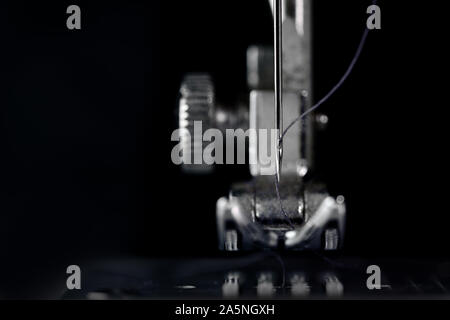 Needle and presser foot of a sewing machine in front view as extreme macro shot, technical invention for the clothing industry, dark background with c Stock Photo