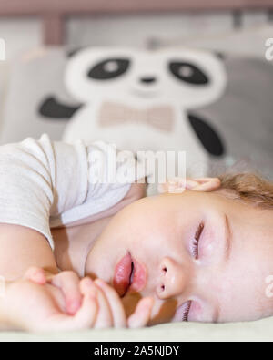 Face of a little girl sleeping on a background of a pillow with a panda, vertical portrait. Baby girl boy Caucasian daytime sleep Stock Photo