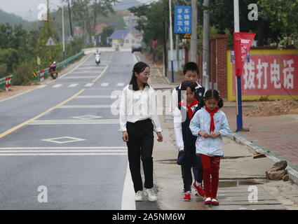 (191022) -- LUOTIAN, Oct. 22, 2019 (Xinhua) -- Fang Rong walks students home in Luotian County, central China's Hubei Province, Oct. 11, 2019. Fang Rong, 29, is the headmaster of Hope primary school of Luotian County, her alma mater. Born in a poverty-stricken region, Fang Rong was a left-behind girl. Thanks to the Hope Project and people's aids, she succeeded in graduating from a secondary normal school. To help more children and repay people's kindness, she decided to be a teacher at her alma mater. In spite of the austere way of life, Fang shouldered her responsibility from various asp Stock Photo