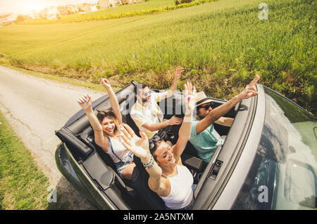 Group of friends having fun at car trip. Four caucasian people on a sportive car with hands up. Stock Photo