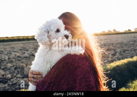 Woman hugging her dog at the field at sunset Stock Photo