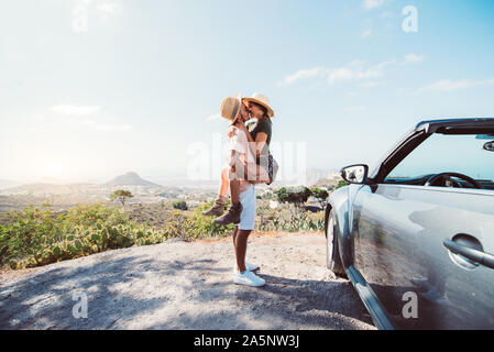 Romantic escape in Tenerife . Couple in love kissing on a cliff at road trip with a convertible car Stock Photo