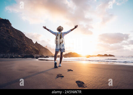 Young man arms outstretched by the sea at sunrise enjoying freedom and life, people travel wellbeing concept Stock Photo