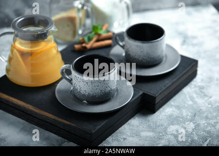 Transparent glass teapot with chitrus tea and cups, tea set on a wooden table. Close up, gray background, soft light Stock Photo