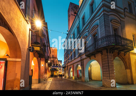 Cobblestone pedestrian street illuminated in evening in Old Town of Alba, Piedmont, Northern Italy. Stock Photo