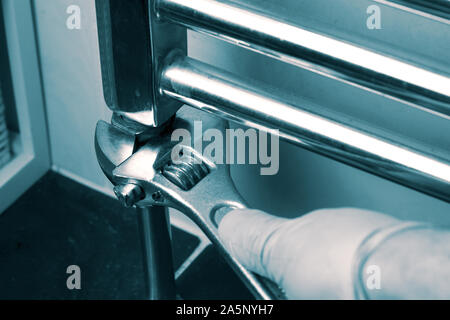 Man installing tightening a nut with a spanner wrench on a modern wall mounted radiator in a bathroom.  With blue toning Stock Photo
