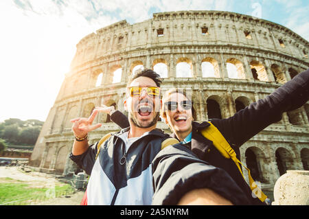 Happy caucasian couple is taking a selfie smiling at the camera in front of the colosseum in Rome Stock Photo