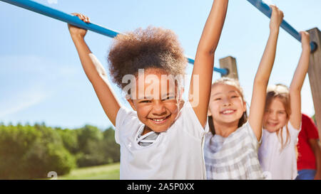 Multicultural kids shimmy on jungle gym on the trim path Stock Photo