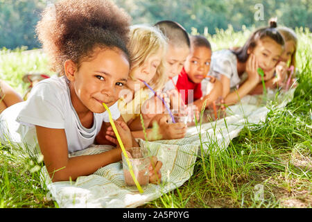 Multicultural children drink water with a straw in the summer in nature Stock Photo