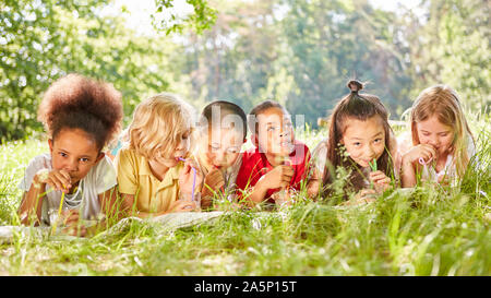 Multicultural children drink water with straw on summer meadow Stock Photo