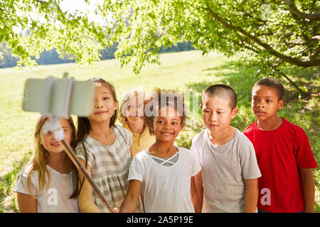 Multicultural group of kids makes selfie with a selfie stick in the nature in summer Stock Photo