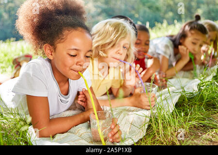 Thirsty multicultural kids drink water with straw on meadow Stock Photo