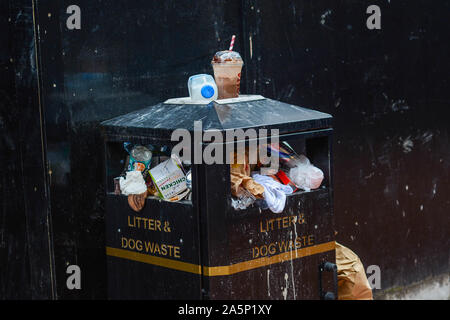 Single use paper cups, plastic bottles, cardboard and another variety of general waste is overflowing from the trash bins Stock Photo