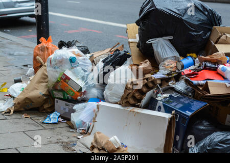 Single use paper cups, plastic bottles, cardboard and another variety of general waste is overflowing from the trash bins Stock Photo