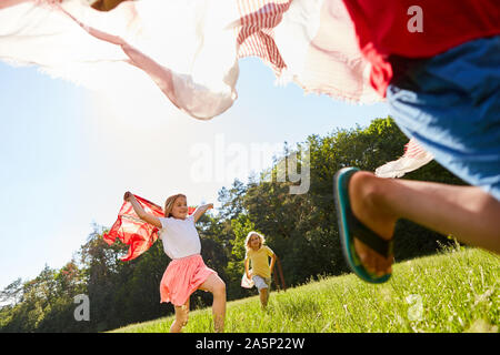 Children play and run with towels on a meadow in nature Stock Photo