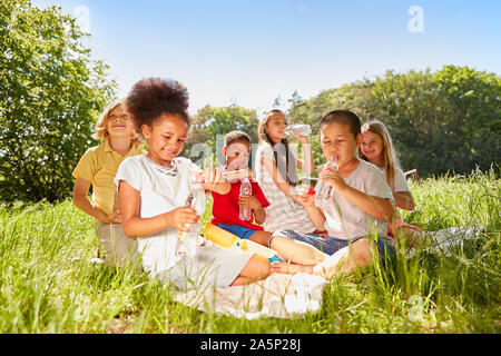 Group of multicultural kids drinks water on a meadow in summer Stock Photo