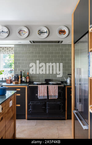 Decorative plates above black AGA with green metro tiles in bespoke kitchen by Dominic Ash. Stock Photo