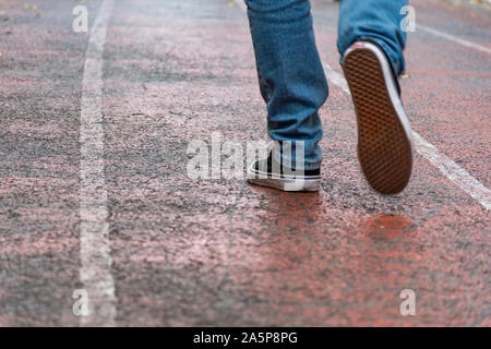 Man wearing jeans and sneaker shoes walking in empty street Stock Photo