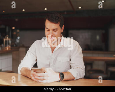 Portrait of a smiling handsome young man at cafe counter using his smart phone Stock Photo